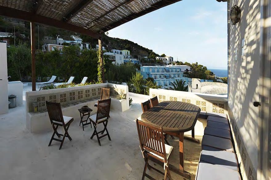 Outdoor dining under the pergola, with the sea beyond.